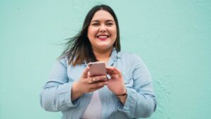 Una donna sorridente con uno smartphone tra le mani.