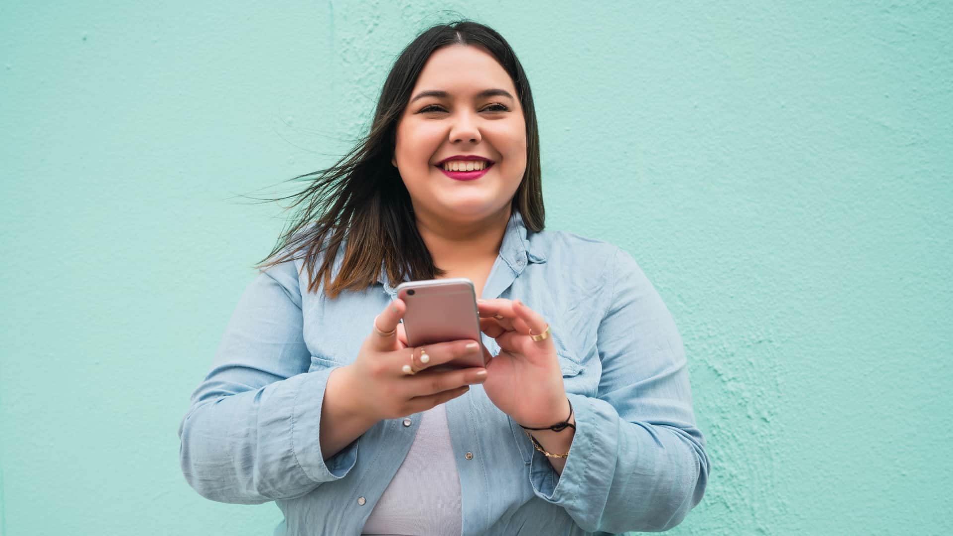 Una donna sorridente con uno smartphone tra le mani.