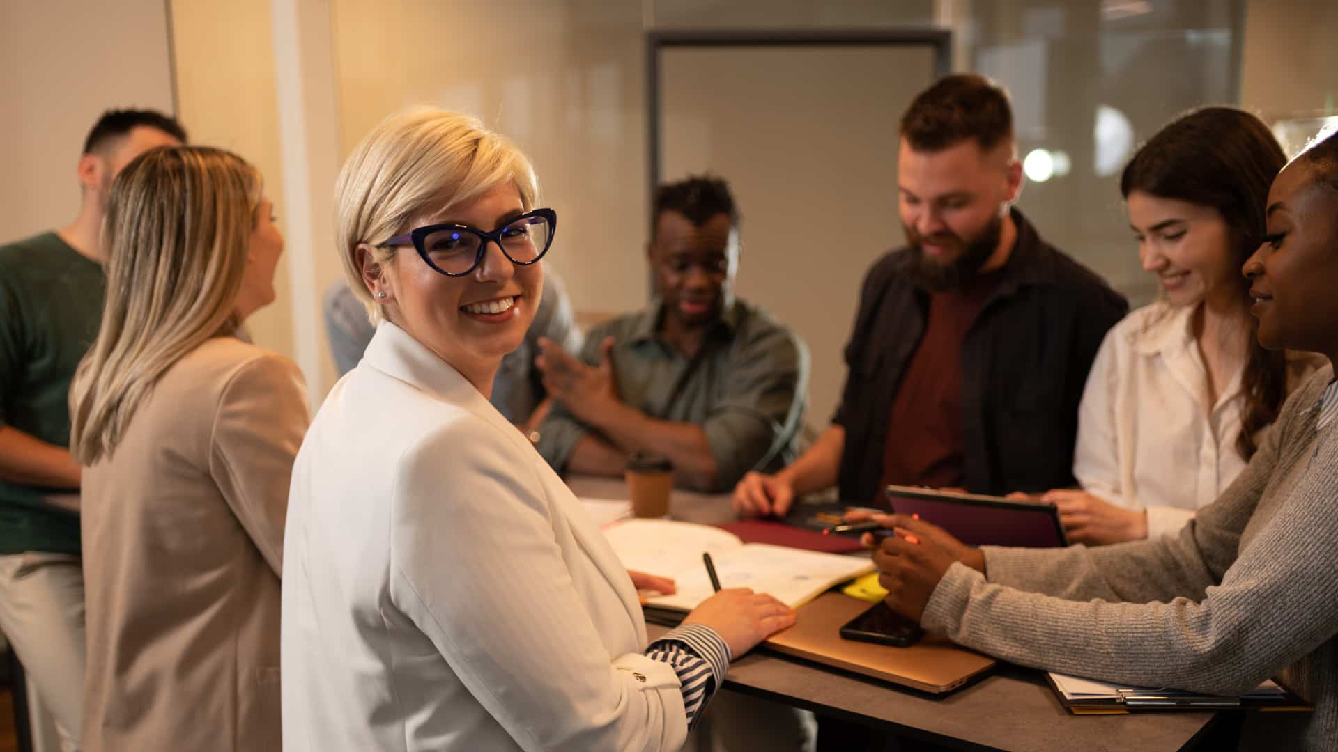 Donna sorridente a un tavolo di lavoro con altri colleghi.
