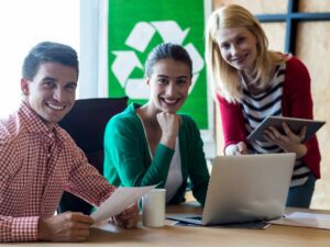 Tre dipendenti di un'azienda di rifiuti, sorridenti alla scrivania davanti a un portatile.