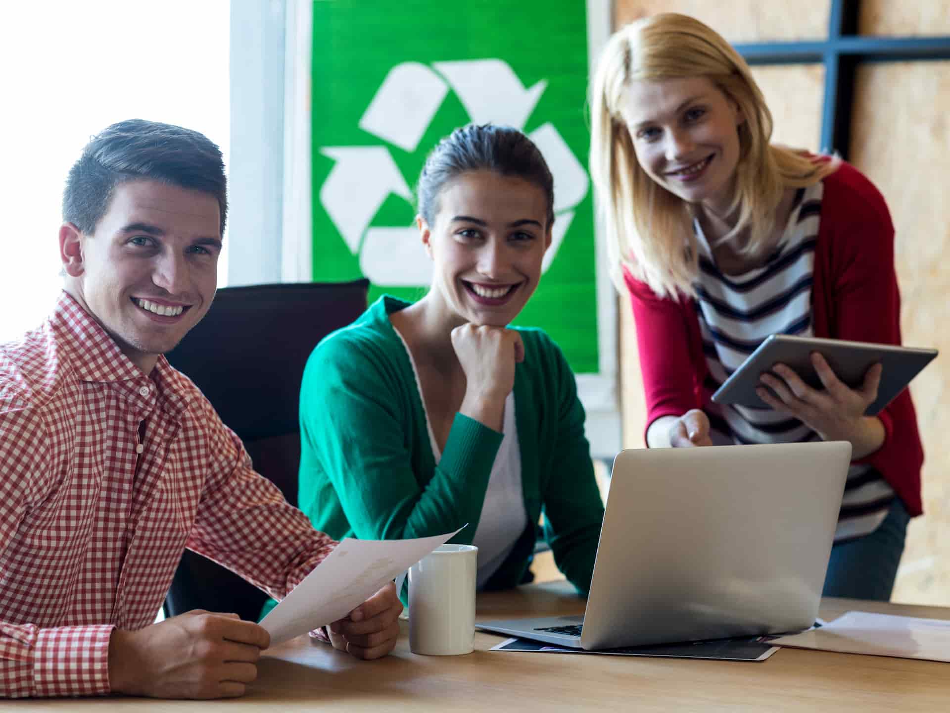 Tre dipendenti di un'azienda di rifiuti, sorridenti alla scrivania davanti a un portatile.